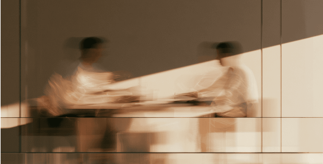 Two people in conversation seen through glass, motion blurred, warm light